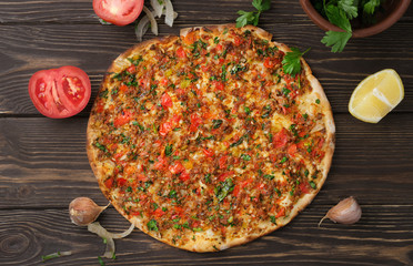 Turkish pizza lahmajun with minced lamb and beef on a thin crust with vegetables and herbs, horizontal layout. Wooden table, top view, flat lay