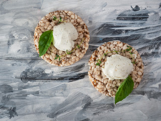A quick light snack, curd cheese with herbs on grain slices with basil leaves on a black and white paper napkin close-up