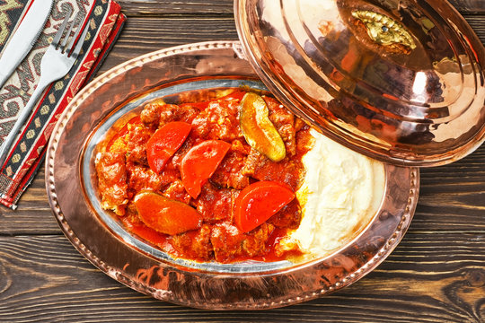 Iskander Kebab is a Turkish dish with meat, spices and vegetables on a traditional copper platter bakir Sahan Kayik) . Wooden dark table, top view, flat lay.