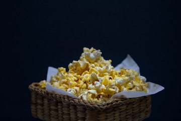 Tasty popcorn in basket on dark background.