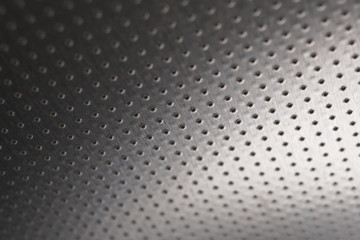 Dark metallic wallpaper or background. Perforated aluminum surface with many holes, hanging from above like a ceiling. Perforation rows go into the distance and form perspective
