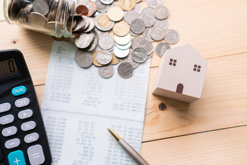 Flat lay of model house, bank book, cash money and calculator on a wooden desk. Home expenses, collect money and investments concept. Top view