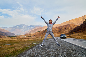 Girl in gray sports clothes on the road in the mountains on a summer or autumn day. A tourist is resting on a trip in nature