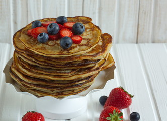 Close-up delicious pancakes, with fresh blueberries, strawberries and maple syrup on a light background. With copy space. Pile of small homemade pancakes with forest fruits.