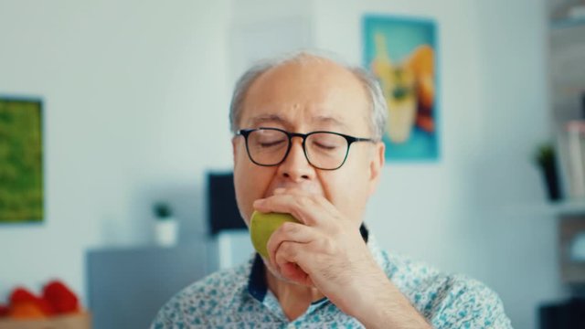 Elderly retired person biting apple during breakfast in mdoern cozy kitchen. Healthy green happy fresh lifestyle with organic food