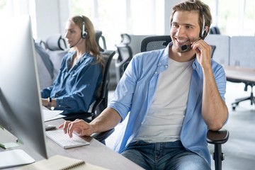 Young handsome male customer support phone operator with headset working in call center.