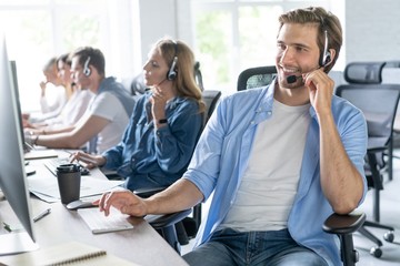 Young handsome male customer support phone operator with headset working in call center.