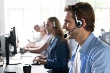 Young handsome male customer support phone operator with headset working in call center.