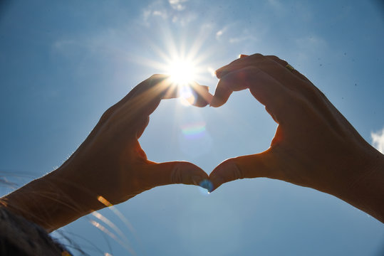 Heart shape universal sign for love and romance. Female hands in the shape of a heart on a background of bright sun