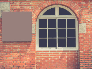 Arched window in a red brick wall with a blank board next to it.