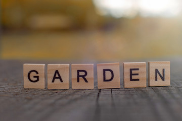 Wooden letter in the word Garden, stands of a gray wooden table with a view of the autumn landscape