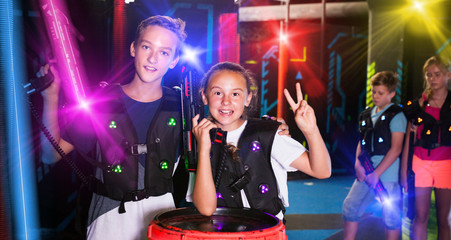 Portrait of happy teenager girl and boy with laser guns on dark lasertag arena..