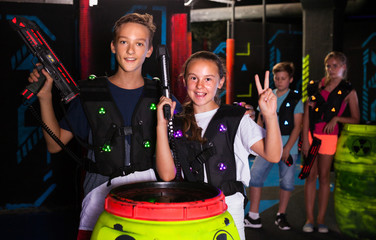 Cheerful teen girl and boy with laser pistols posing together in laser tag labyrinth..