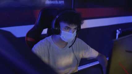 Close up of Young Gamer in face mask plays in Online Video Game in Modern computer club.
