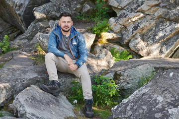 Naklejka na ściany i meble Portrait of mature man in casual clothing sitting on rocks and looking at camera during hiking