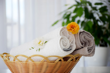 Fototapeta na wymiar Fresh gray and white towels rolled in wicker bascket decorated with flowers and liquid container. Spa and wellness, massage or beauty salon, laundry or dry-cleaning concept 