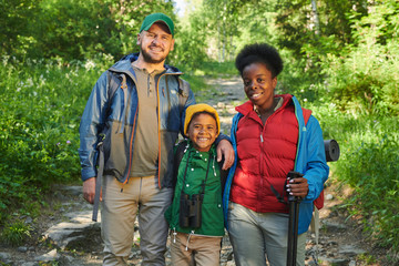 Portrait of happy family of tourists standing in the forest and smiling at camera