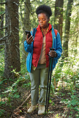 African woman using her mobile phone while go hiking in the forest