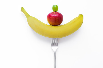 Yellow banana Red apple and green grapes on a fork fresh juicy raw fruits. Vegetarian and vegan...