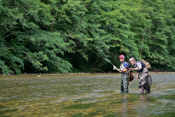 A father and his son fly fishing in summer on a beautiful trout river with clear water