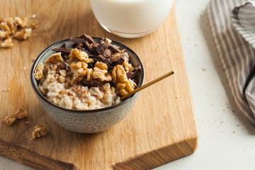 Oatmeal porridge with nuts, chocolate in a gray bowl, a glass of milk. Breakfast, healthy food. Good morning.