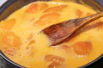 Wooden spoon in foam when cooking apricot jam in a saucepan
