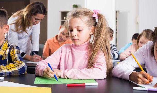 Girl and children in elementary age at drawing lesson together