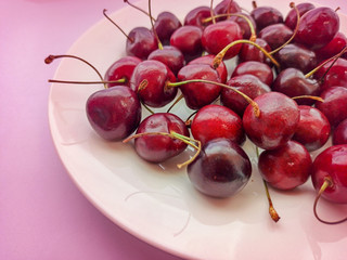 Close-up sweet cherries on a plate on a pink background. Ripe red berries. Selective focus