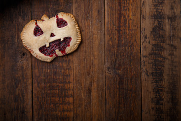 Pies with carved scary faces. Happy Halloween recipe. Homemade cake with red berries and pumpkin tart on wooden table.  Top view. Copy space.