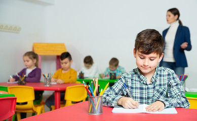 Fototapeta premium Portrait of little assiduous boy with pen and notebook at lesson in elementary school. High quality photo