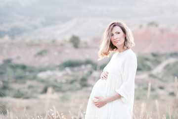 Fototapeta na wymiar Pregnant woman wearing dress posing outdoors over nature background. Motherhood. Maternity. Healthy lifestyle. Happiness.