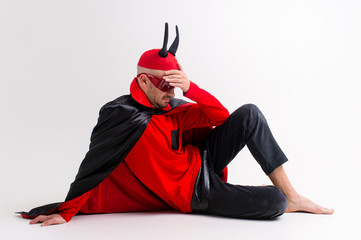 Strange man in masquerade clothes and red hat with black horns posing over white background.