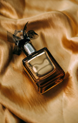 Perfume bottle on golden satin fabric, close-up, warm light. 