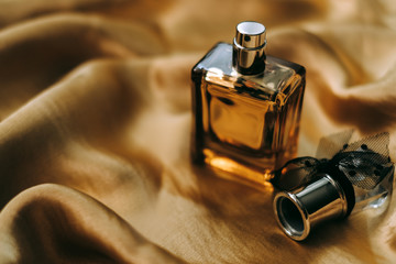 Perfume bottle on golden satin fabric, close-up, warm light. 