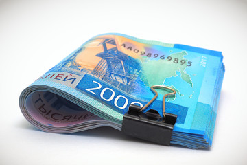 A rolled-up bundle of Russian 2000-ruble banknotes. Money tied with an office clip and lie on a white paper background. Vignetting. Child support allowance and unemployment benefit in Russia. Macro