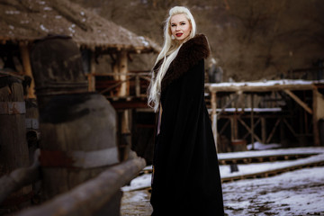 Beautiful blonde Viking dressed in a black cloak against the backdrop of the castle