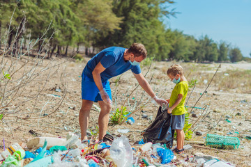 Volunteers in blue face mask. Father, son pick up garbage which pollute beach near lazur sea....