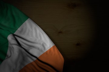 nice dark image of Ireland flag with big folds on dark wood with free place for text - any holiday flag 3d illustration..
