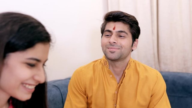 Young siblings in traditional wear celebrating Raksha Bandhan/Bhai Dooj festival. Beautiful Indian girl happily performing the ceremony of putting tika on her brother's forehead - Raksha Bandhan/Bh...