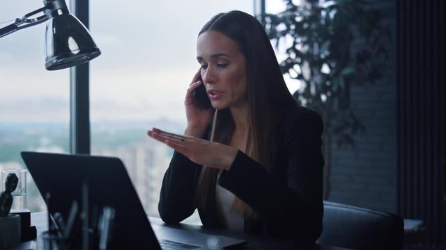 Businesswoman talking on smartphone in office. Woman looking at laptop screen