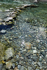 Bergfluss mit großen Steinen im Flussbett und Reflexionen der Sonne