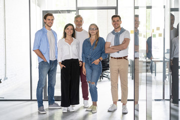 Young modern colleagues in smart casual wear looking at camera standing in the creative office.