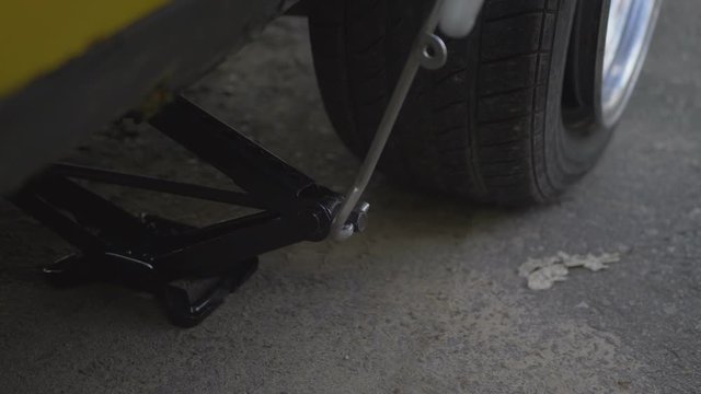 A Man With A Lifting Jack Lifts A Yellow Car With A Flat Tire. Close-Up Time Lapse