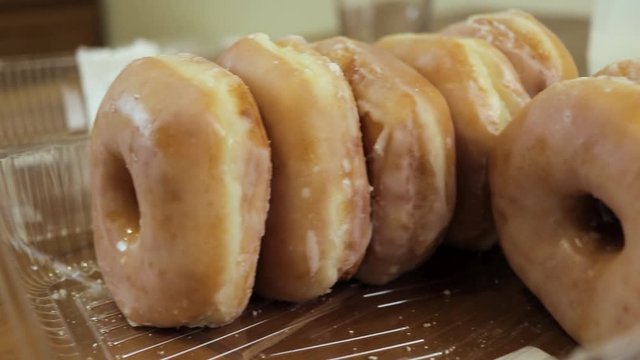 A Panning Shot Of Box Of Glazed Donuts On A Table With Some Milk.