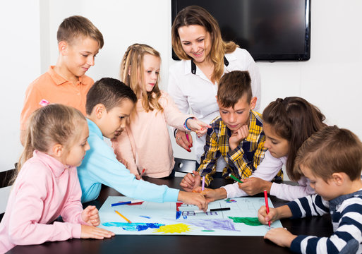 Portrait smiling team of elementary age children and teacher drawing on one sheet