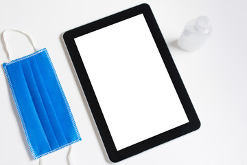 Flat lay of a tablet next to face mask and hand sanitizer - concept of disinfecting items
