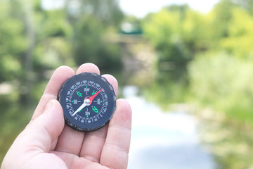 Old classic navigation compass in hand on natural background as symbol of tourism with compass,...