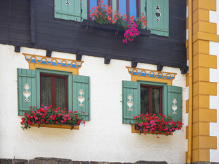 Facade of traditional austrian house with ancient wooden windows and blinds or shutters. Colorful geraniums hang from the window.