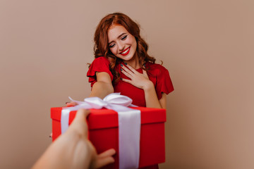 Pleased red-haired woman enjoying christmas presents. Studio photo of interested smiling girl celebrating new year.