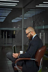 Businessman in a blue shirt sitting in a brown leather chair. Man in a jacket with a laptop in glasses. Bearded office worker with a white cup of coffee.